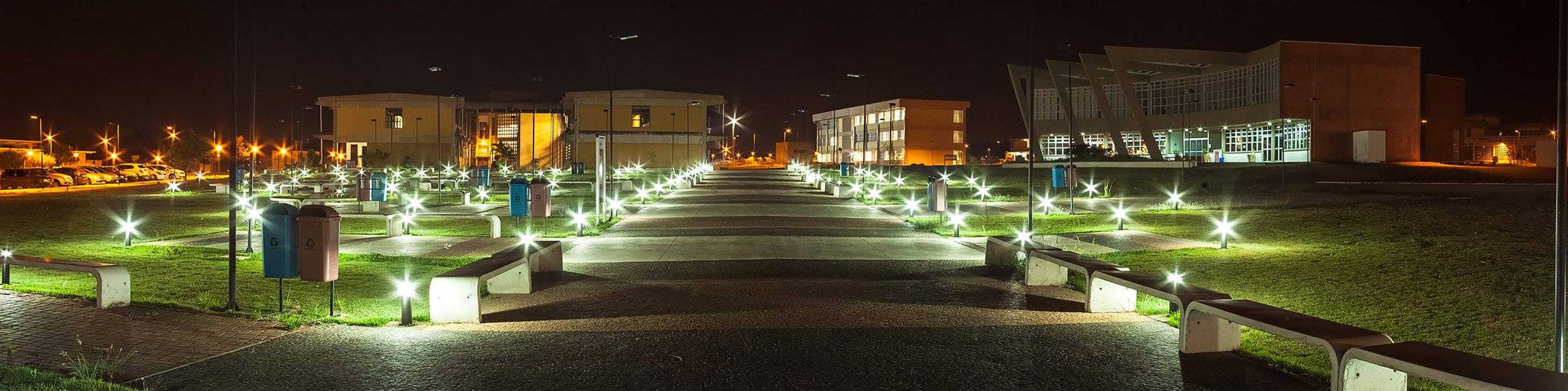 Caminho à noite, adornado com luzes no chão, com destino aos prédios localizados na área norte da UFSCar campus São Carlos, oferecendo uma experiência visual agradável e iluminada.