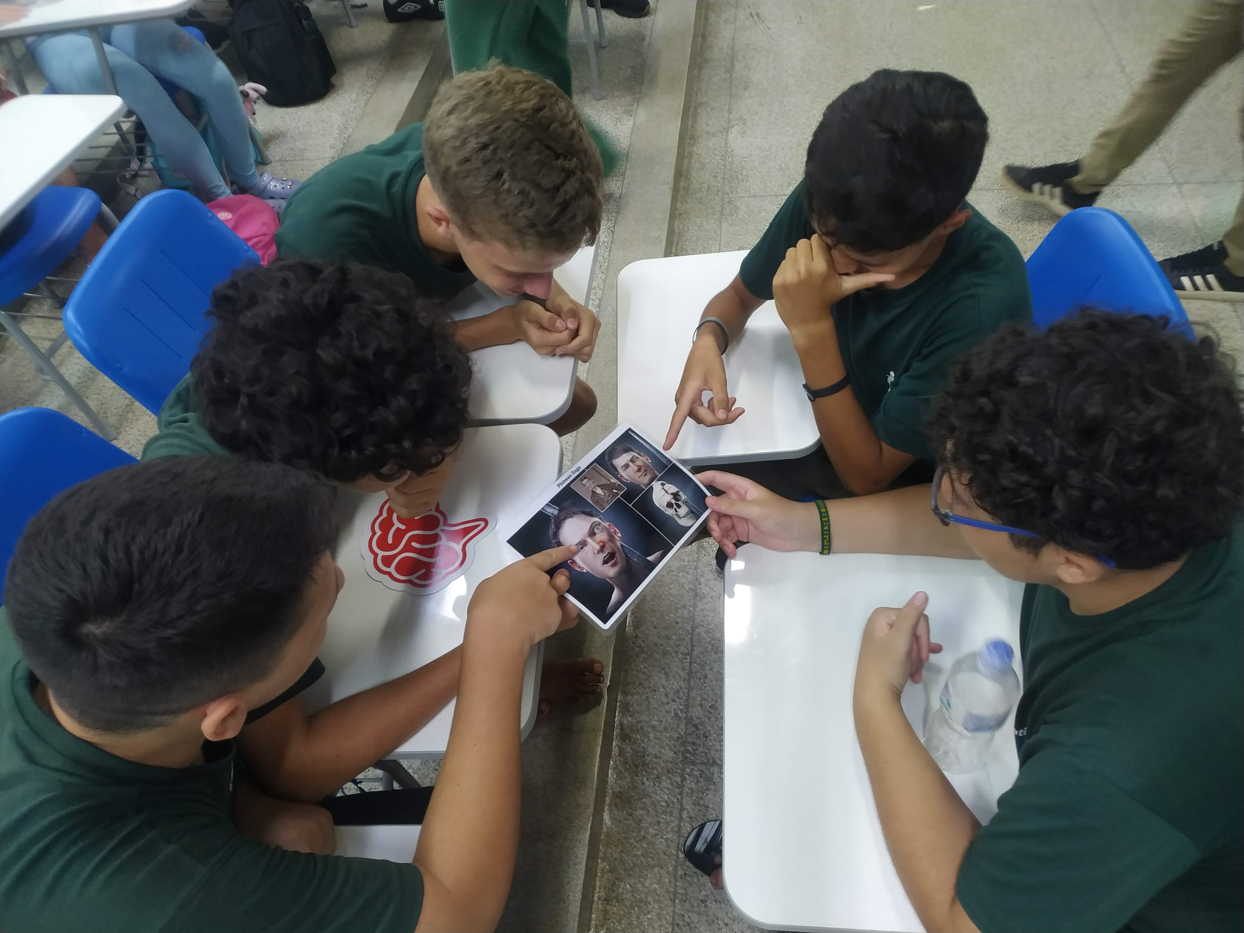 13/03/2024- Palestra proferida pela professora Márcia Cominetti na escola Educativa, em São Carlos, sobre envelhecimento e evidências científicas sobre o funcionamento do cérebro e demências. Na imagem vemos 5 estudantes, vestidos com o uniforme camiseta verde da escola, reunidos em roda, analisando uma imagem trazida pela professora Márcia Cominetti para ilustrar sua fala. Dois estudantes apontam para a imagem que retrata o caso de Phineas Gage, com a reprodução simulada 3d do acidente em que uma barra de ferro atravessou seu crânio.